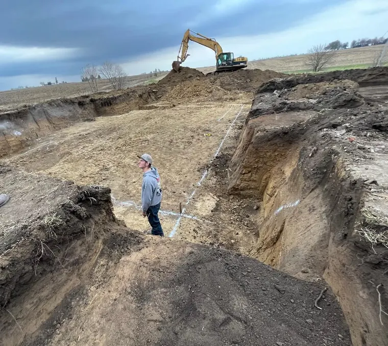 Basement excavation dug and squared with footing lines marked, excavator working the soil pile behind, Farmington, Illinois