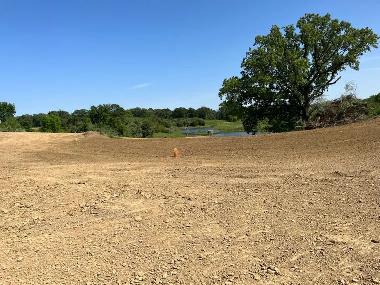 Cleared and graded ground sloping to a farm pond after tree removal and field tile work in Elmwood, Illinois