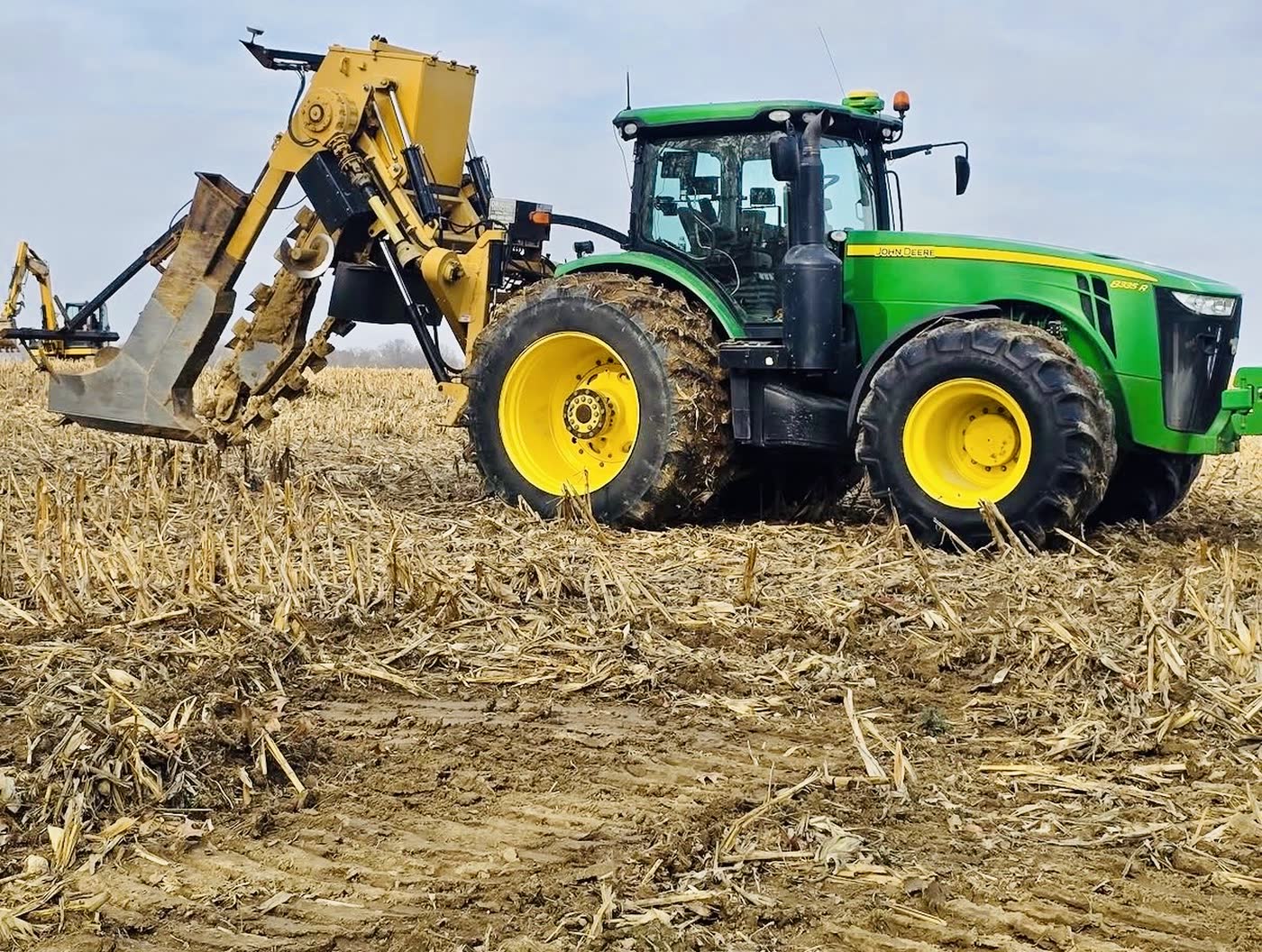 John Deere tractor pulling a tile plow through corn stubble, installing field tile on central Illinois farm ground