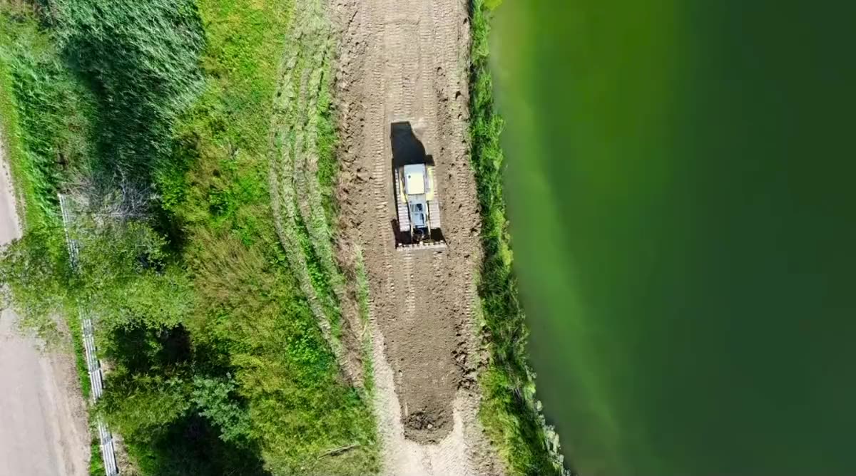 Aerial view straight down on a dozer pushing pond soil back off the water along a rebuilt bank, central Illinois