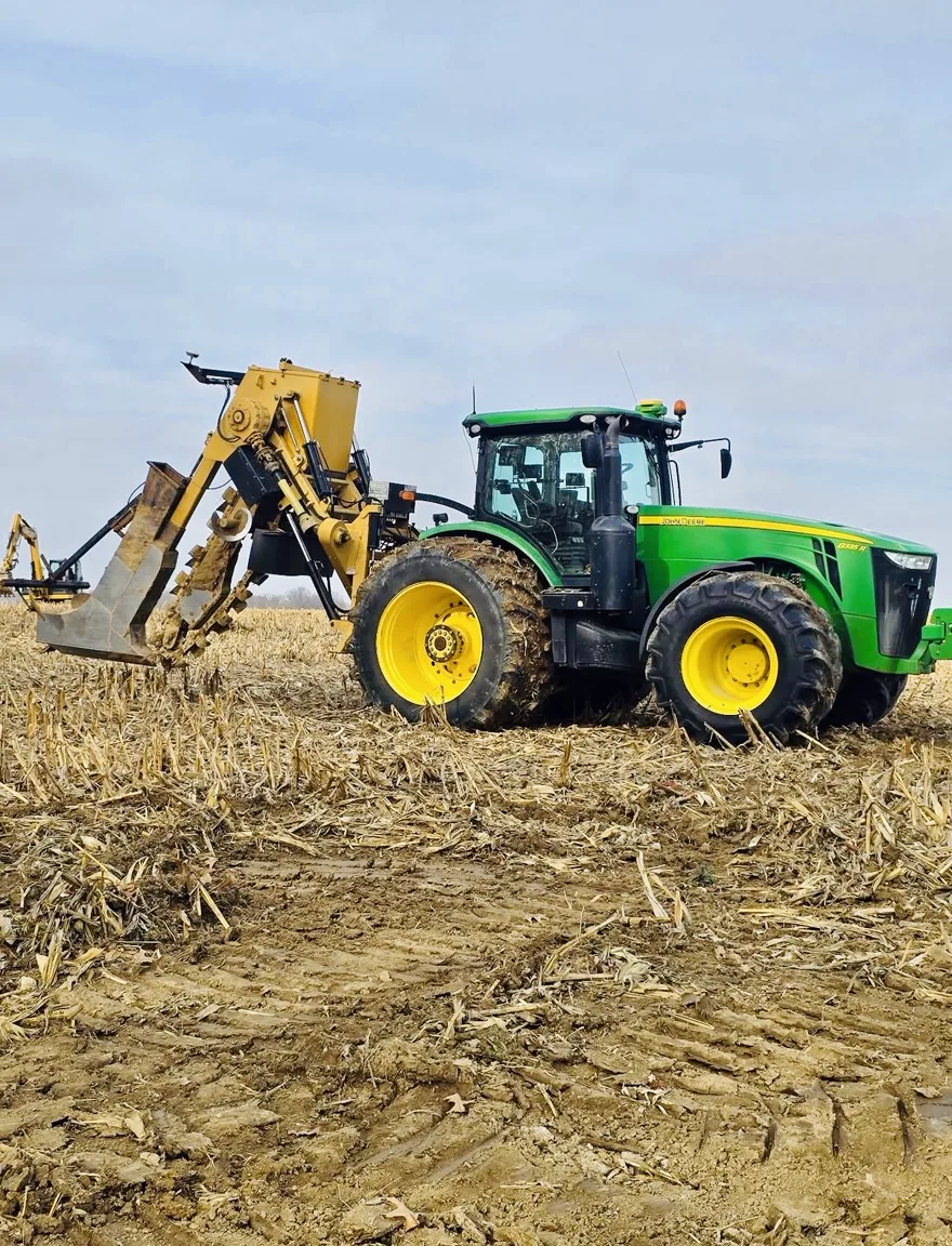 Green tractor with a yellow tile plow on harvested corn ground in central Illinois